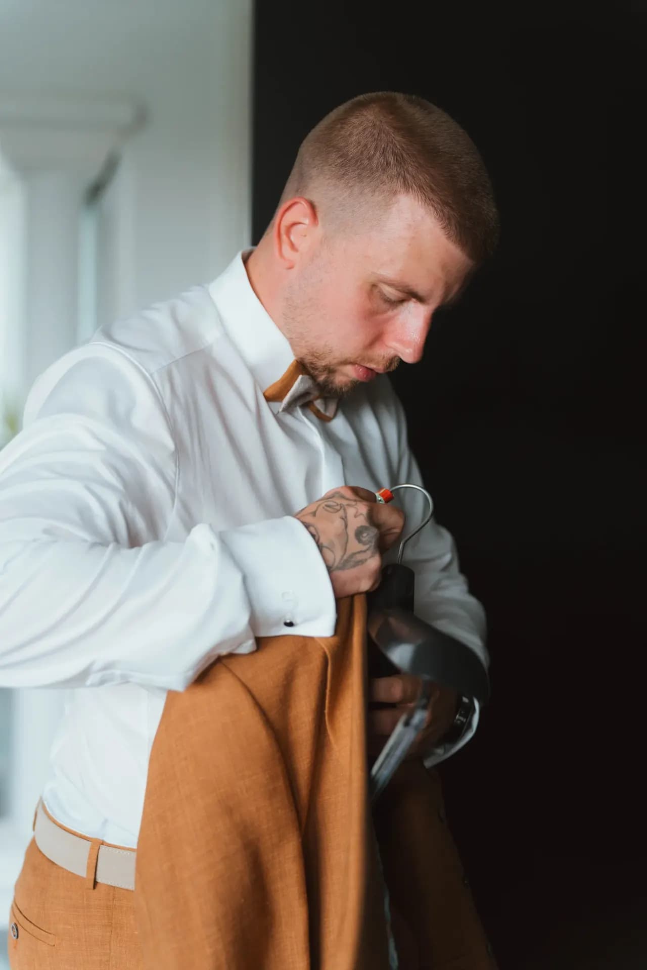 Bräutigam mit Tattoos richtet konzentriert seine cognacfarbene Krawatte